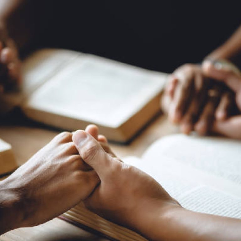 Christian group of people holding hands praying worship to believe and Bible on a wooden table for devotional or prayer meeting concept.